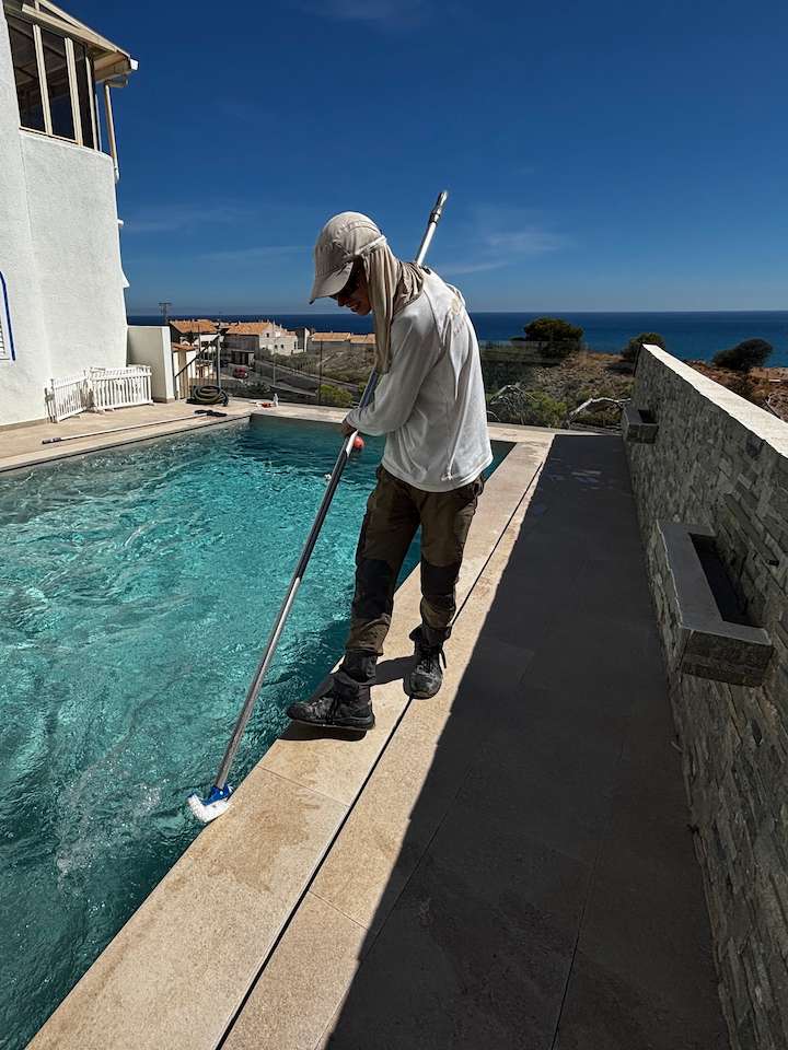 Pool technician brushing the waterline and walls of a swimming pool during routine maintenance